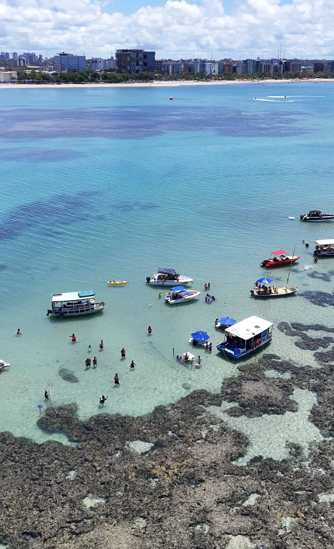 Vista aérea das piscinas naturais próxima à orla de Maceió com barcos ancorados