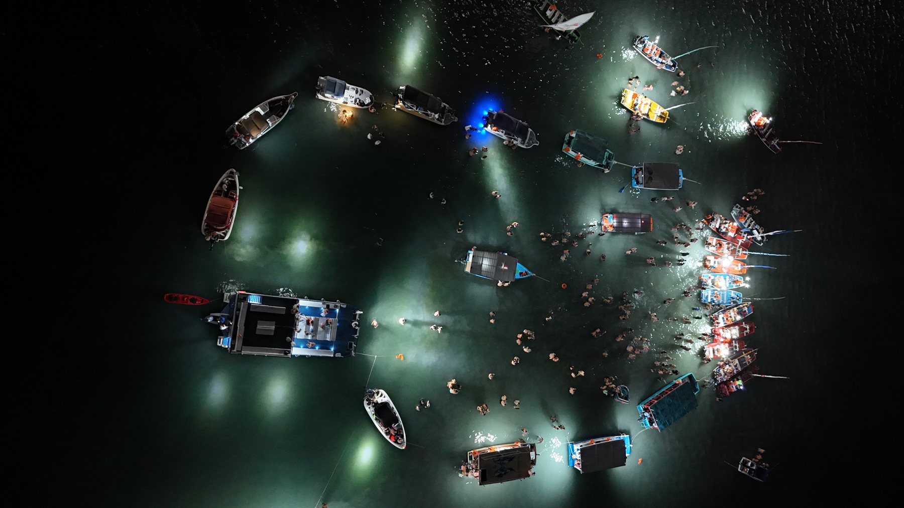 Vista aérea noturna do banho de lua — barcos em círculo iluminando a água escura na Ponta Verde, Maceió