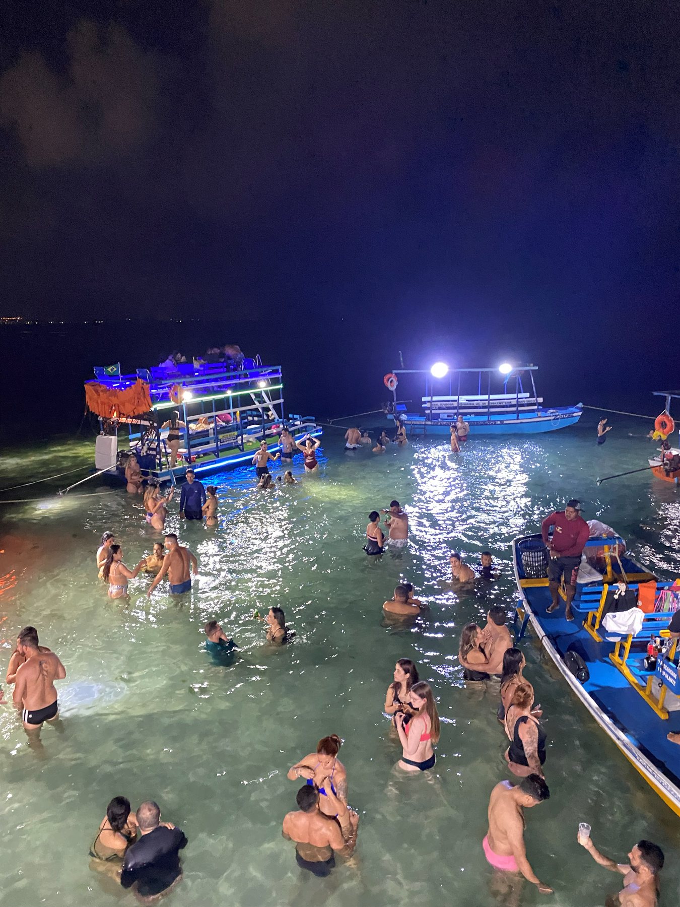 Banhistas curtindo o banho de lua à noite ao redor dos barcos iluminados na Ponta Verde